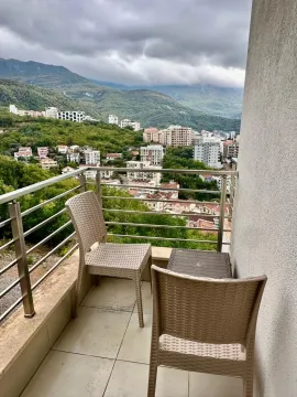 Small furnished balcony with seating set and a view of the city and mountains. - image 10