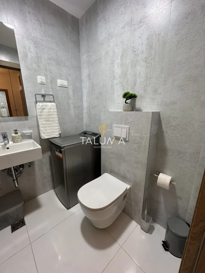 Moderne kupatilo sa sivim pločicama, umivaonikom, WC šoljom i veš mašinom.