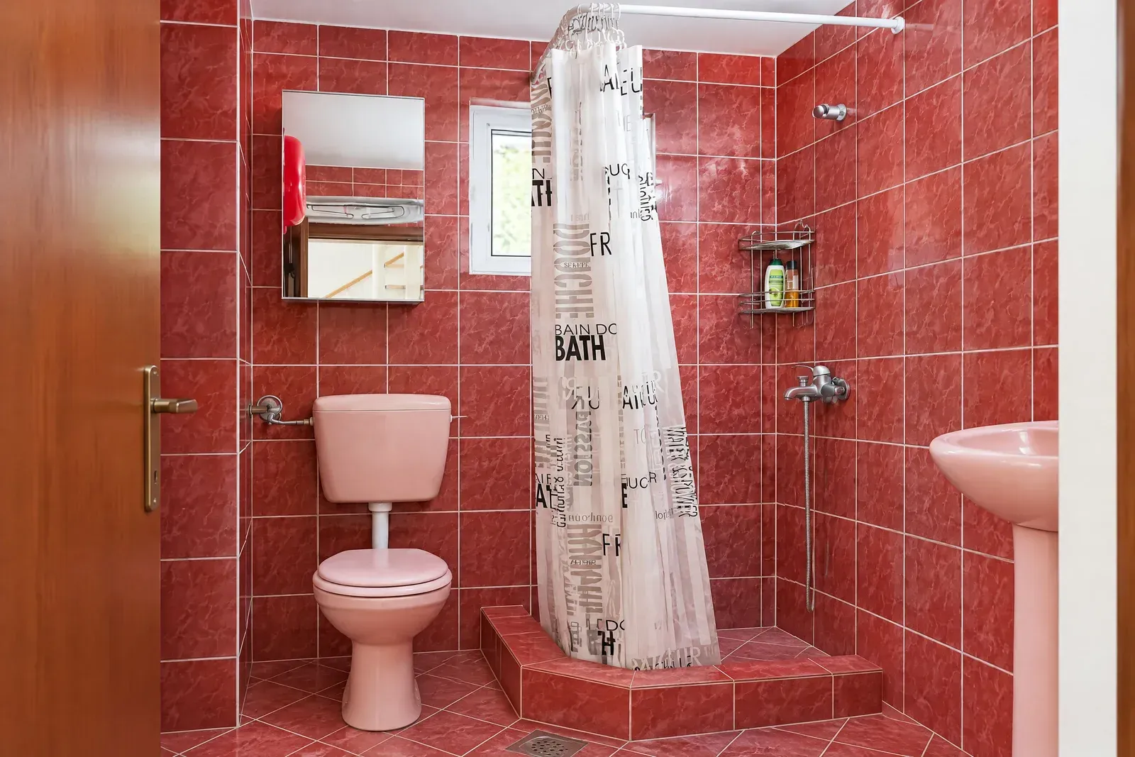 Kupatilo sa crvenim keramičkim pločicama i roze sanitarijama.