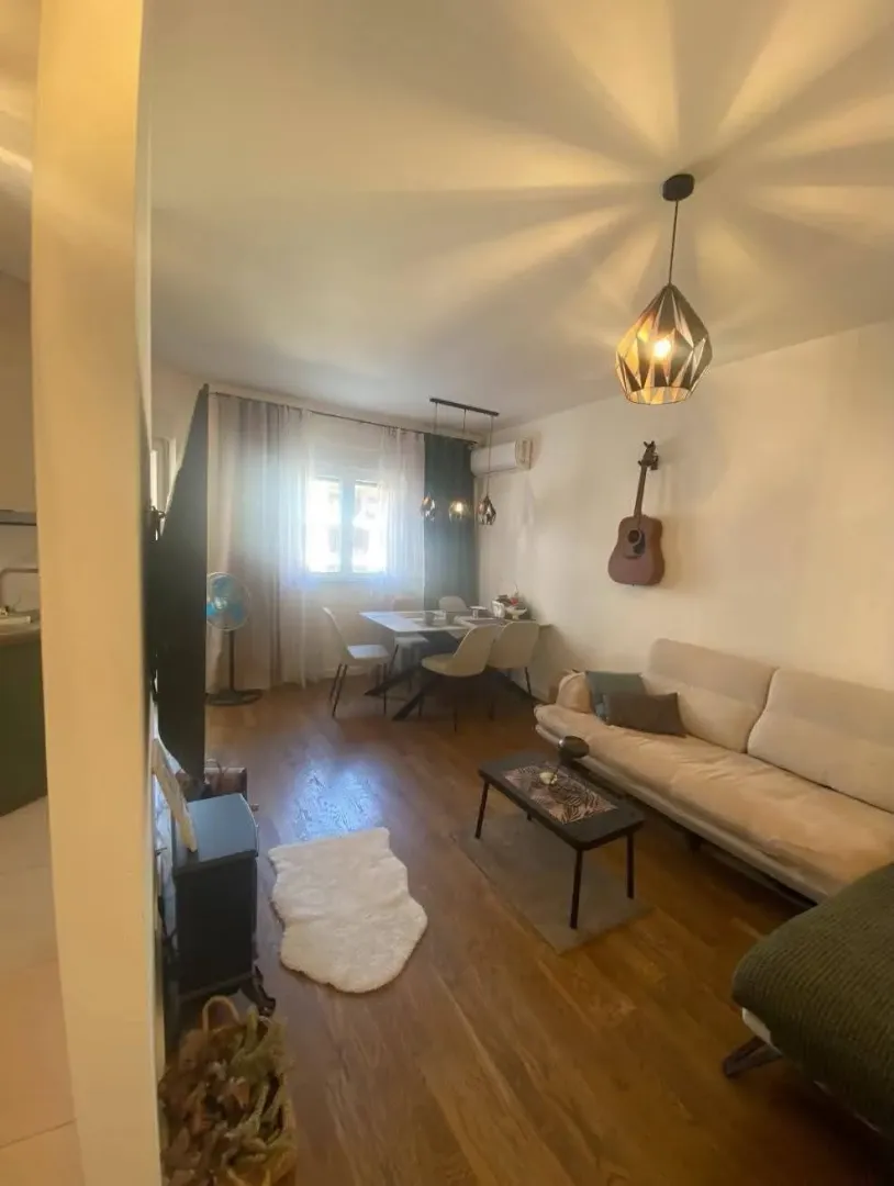 Dnevna soba sa garniturom, stočićem i trpezarijskim stolom u uglu.