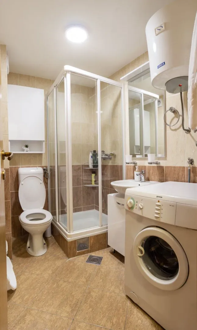 Compact bathroom with a shower cabin, sink, toilet, and washing machine.