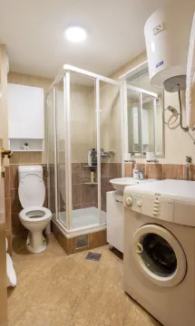 Compact bathroom with a shower cabin, sink, toilet, and washing machine. - image 8