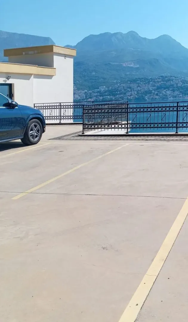 Parking prostor ispred zgrade sa pogledom na more i planine.