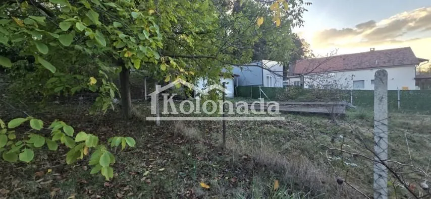 Pogled na dvorište i okolne objekte sa drvećem i ogradom.