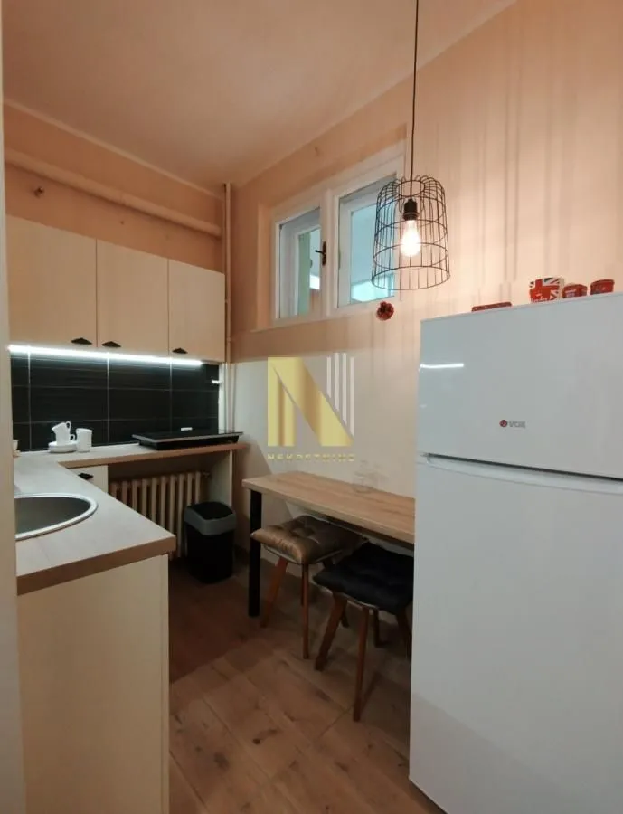 Manja opremljena kuhinja sa frižiderom i trpezarijskim stolom sa stolicama.