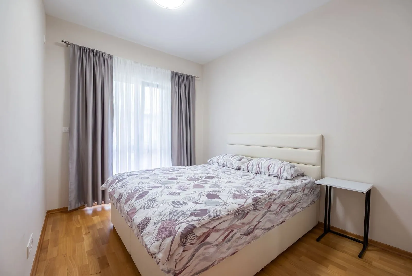 Bright bedroom with a double bed and a window with curtains.