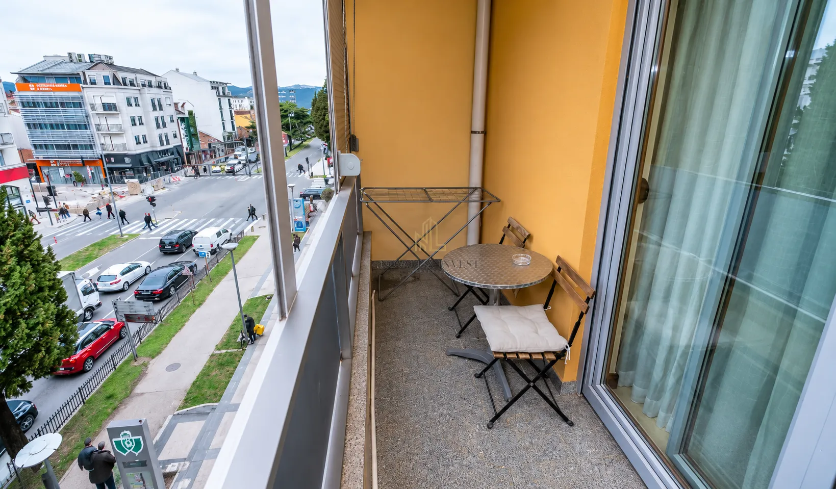 Manji namješten balkon sa stolom, stolicama i sušilicom za veš i pogledom na ulicu.