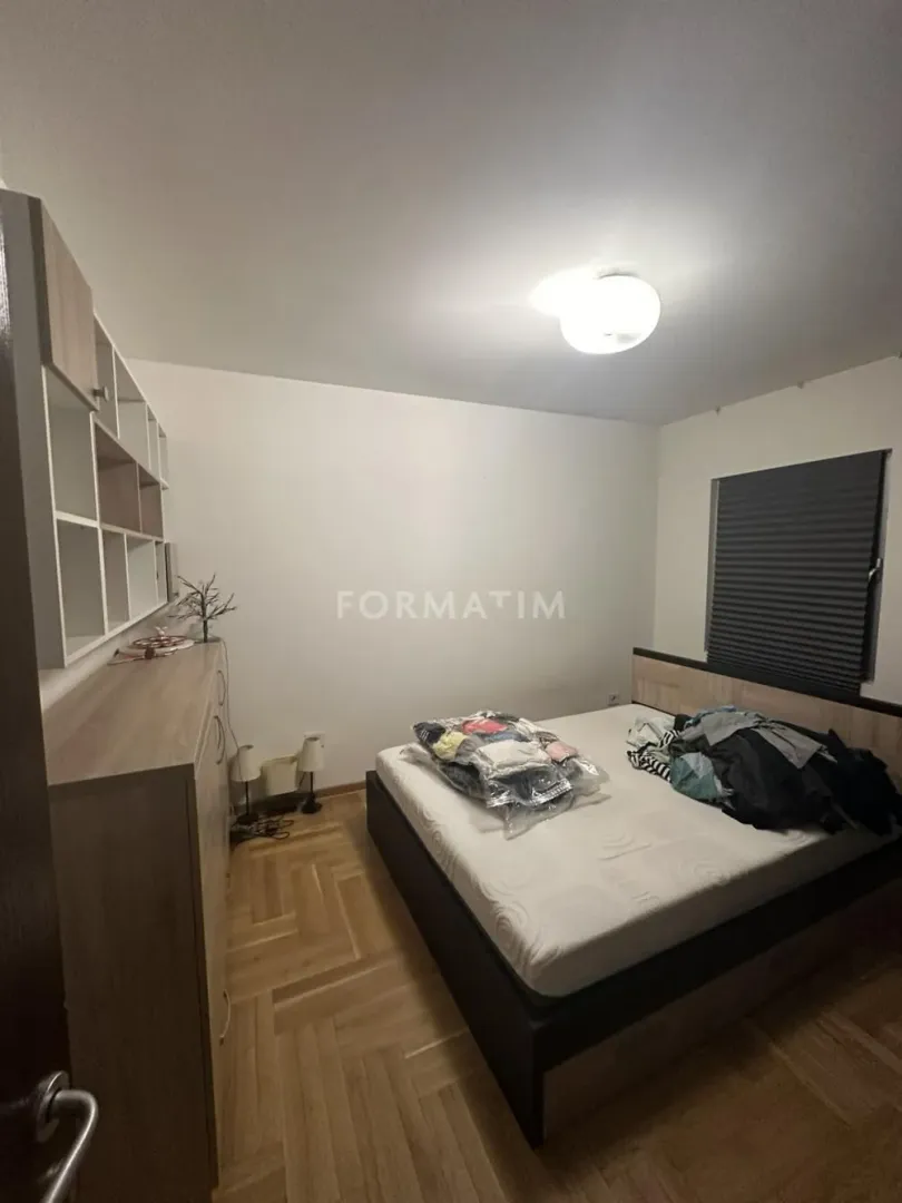 Bedroom with a double bed, wooden parquet flooring, and a dresser with shelving.