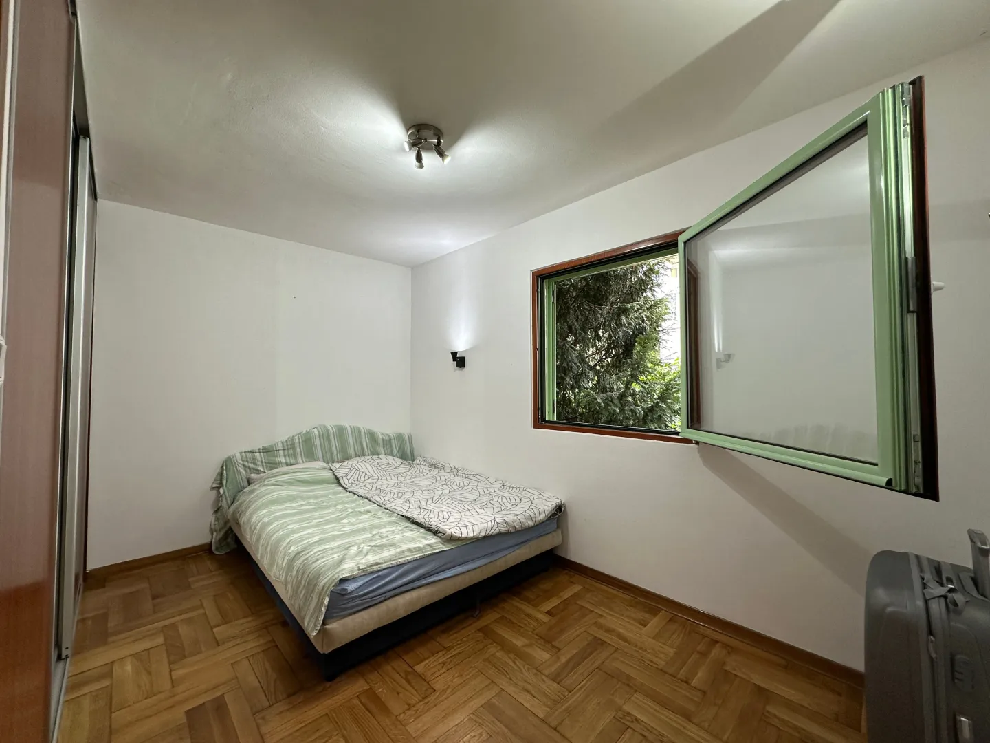 Bedroom with a double bed, parquet flooring, and an open window.