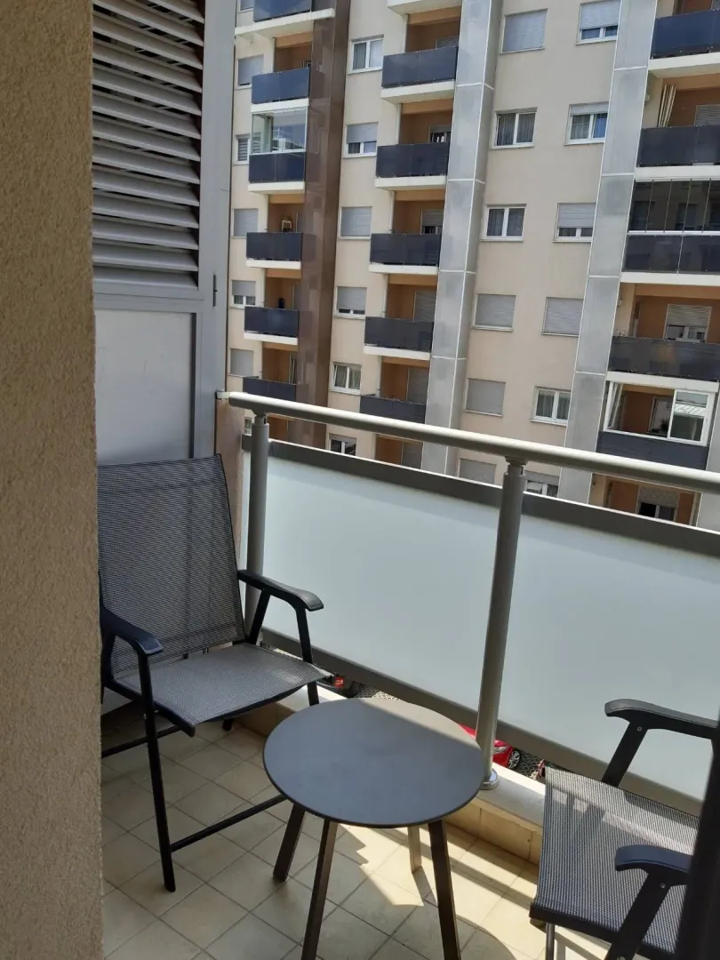 A balcony with two chairs and a table overlooking a neighboring building.