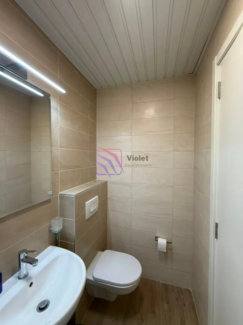 Compact bathroom with a washbasin and toilet in beige tiles.