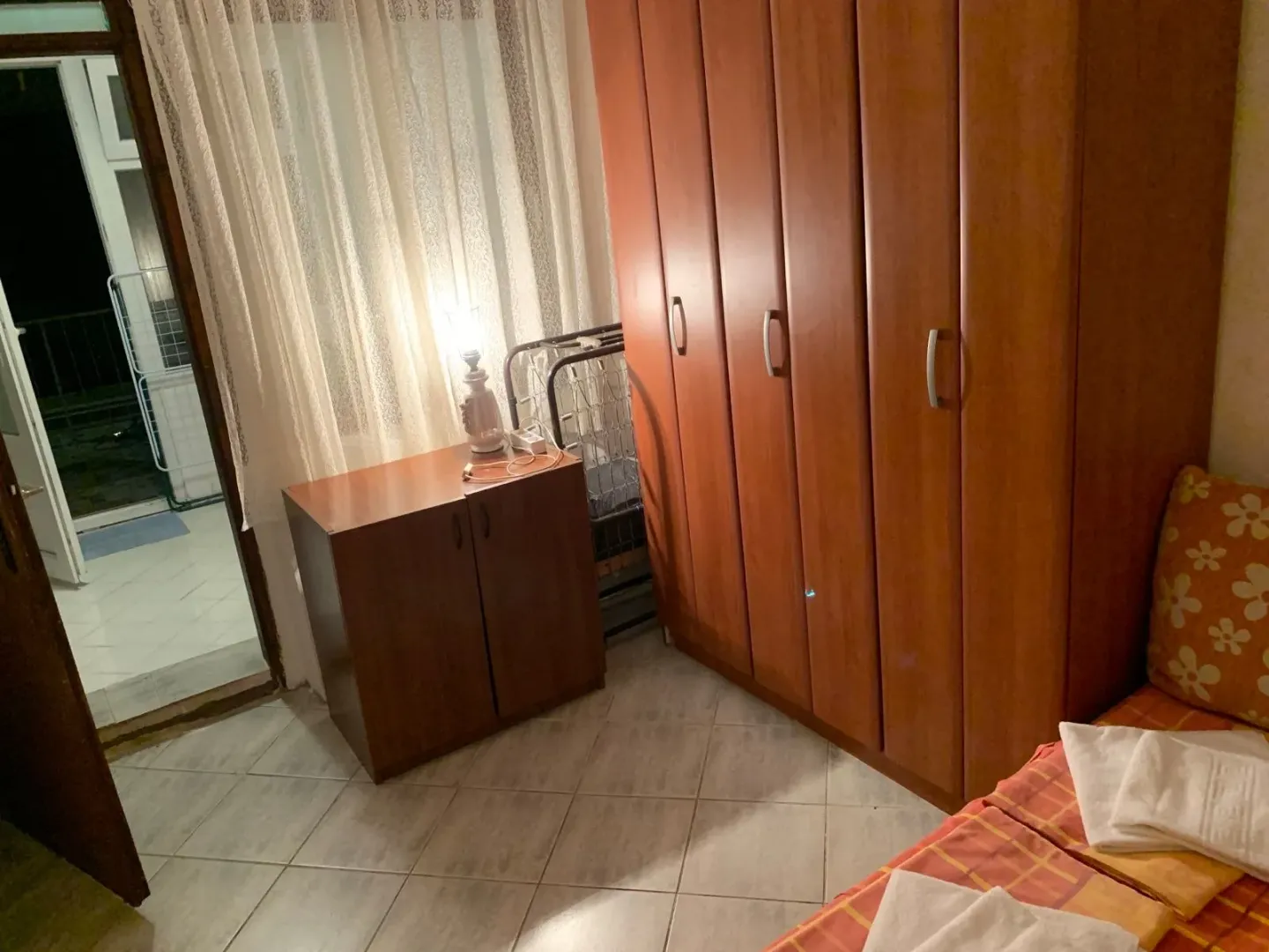 Spavaća soba sa velikim drvenim ormarom, krevetom i izlazom na terasu.