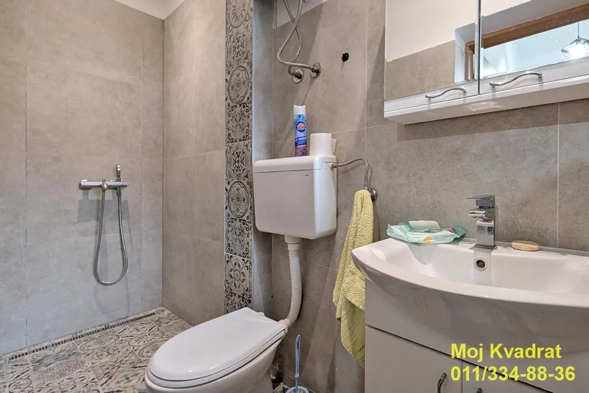 Bathroom equipped with a shower cabin, washbasin, and toilet with grey tiles.