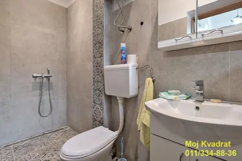 Bathroom equipped with a shower cabin, washbasin, and toilet with grey tiles. - image 6
