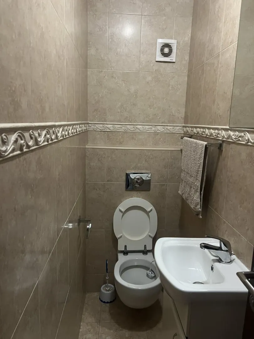 Mali toalet sa umivaonikom i bež pločicama.