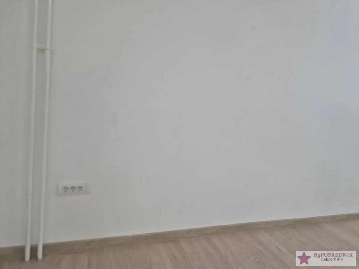 Empty wall with laminate flooring and electrical outlet.