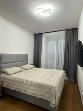 Sređena spavaća soba sa bračnim krevetom, sivim zavjesama i TV-om na zidu. - image 8