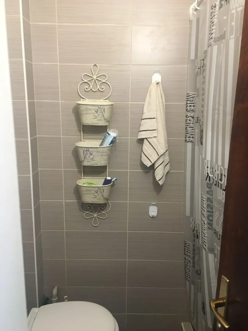 View of the bathroom with ceramic tiles, toilet, and hanging storage shelves.