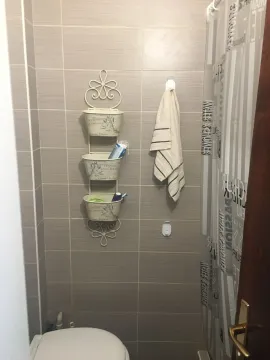 View of the bathroom with ceramic tiles, toilet, and hanging storage shelves. - image 7