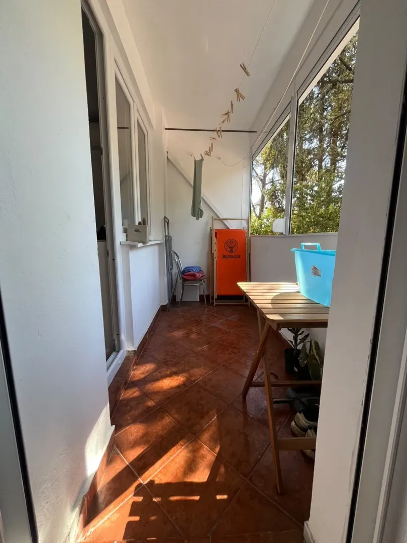 Zastakljeni balkon sa drvenim stolom i pločicama na podu.