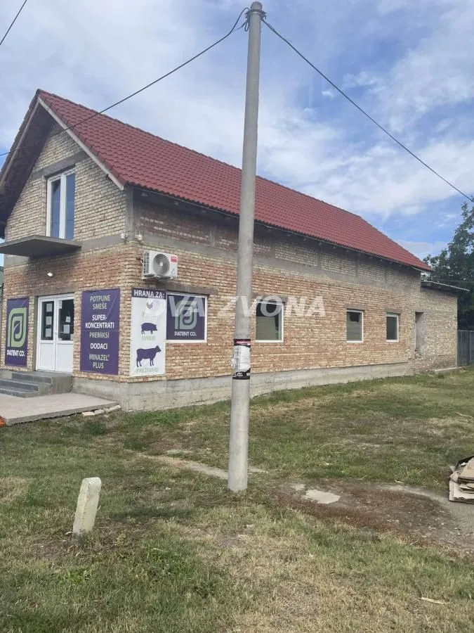 Pogled na spoljašnjost dvospratne kuće sa fasadnom ciglom i poslovnim prostorom u prizemlju.