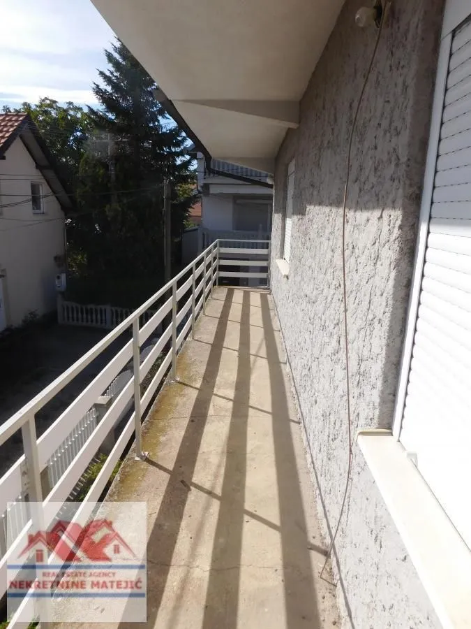 Dugačak balkon sa metalnom ogradom i pogledom na okolne kuće.