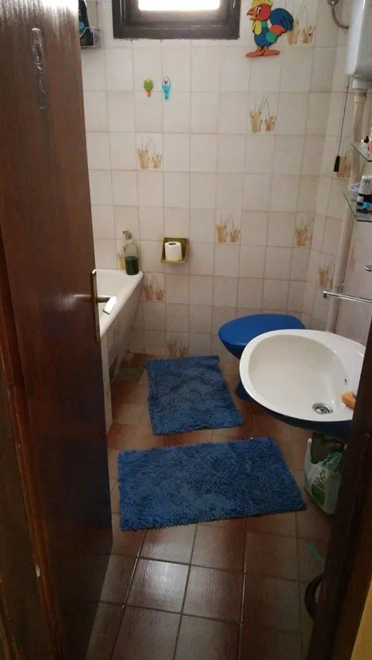 Jednostavno kupatilo sa kadom, umivaonikom i plavim prostirkama.