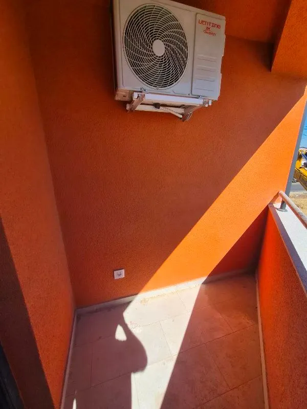 Manji popločani balkon sa spoljnom jedinicom klima uređaja na narandžastom zidu.