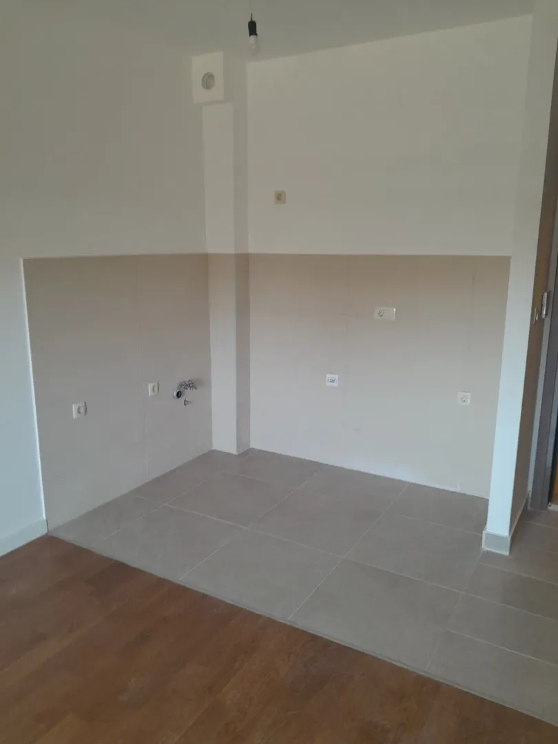 An empty corner of a room with floor and wall tiles and utility connections.