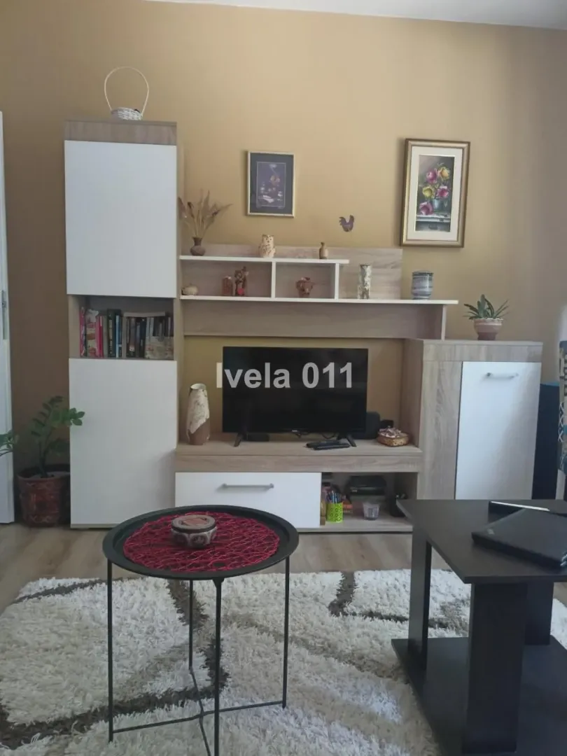 Dnevna soba sa TV elementom, policama i stočićem.