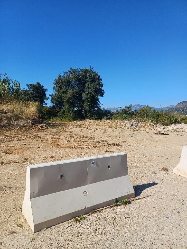Pogled na plac sa rastinjem i betonskom preprekom u prvom planu.