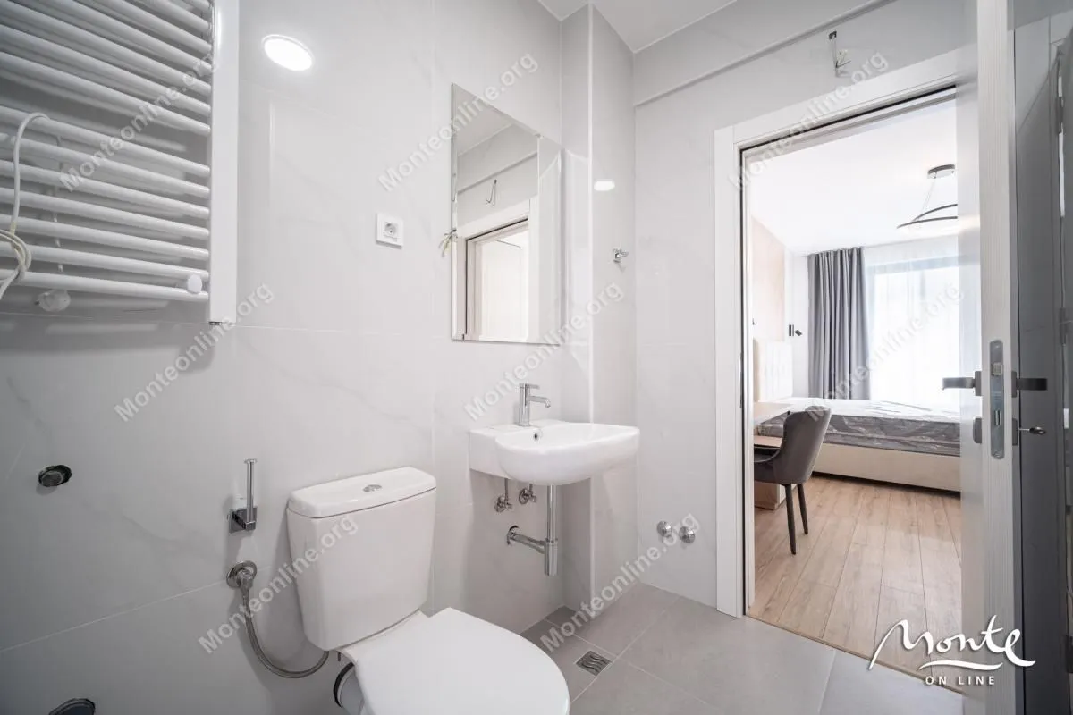 Moderne kupatilo sa umivaonikom, WC šoljom i radijatorom, sa pogledom na spavaću sobu.
