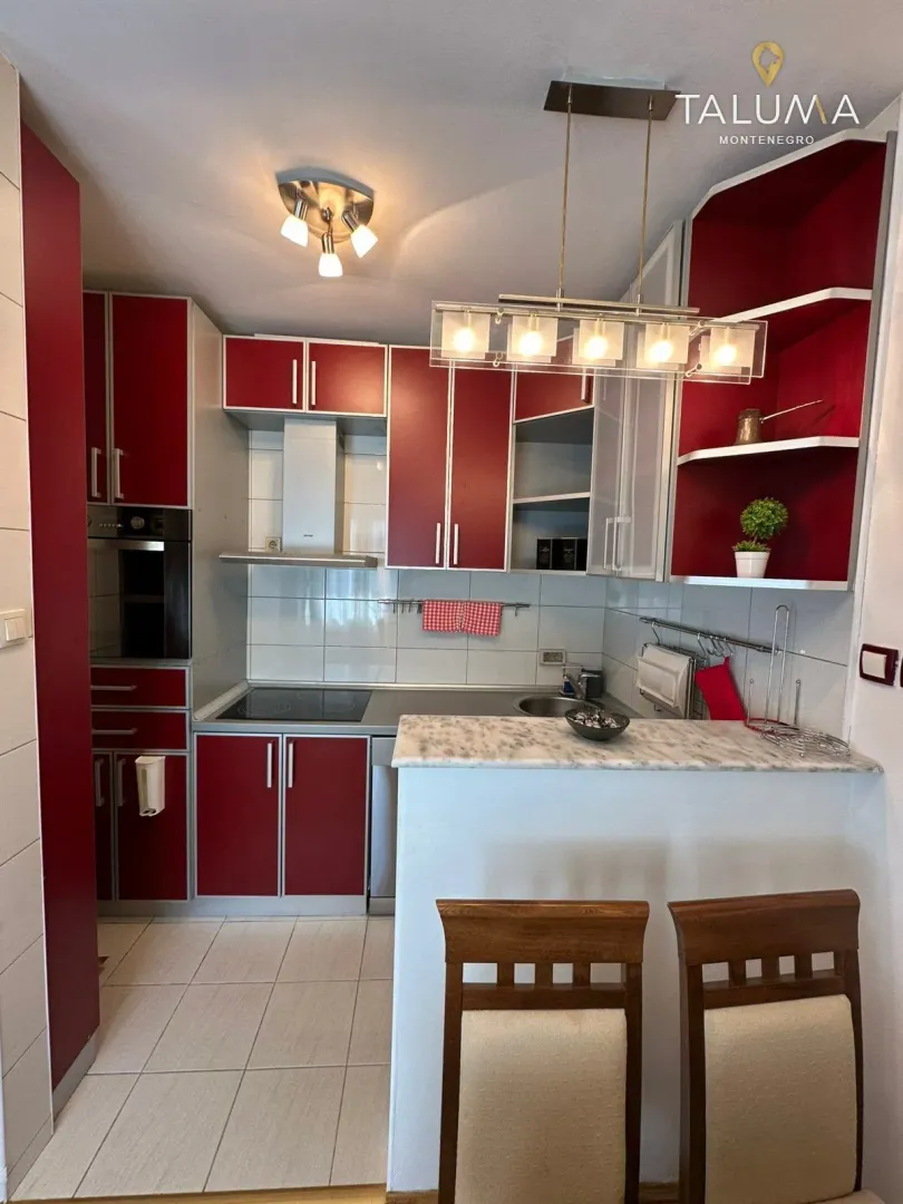 Kitchen equipped with red cabinetry and a bar counter with dining chairs.