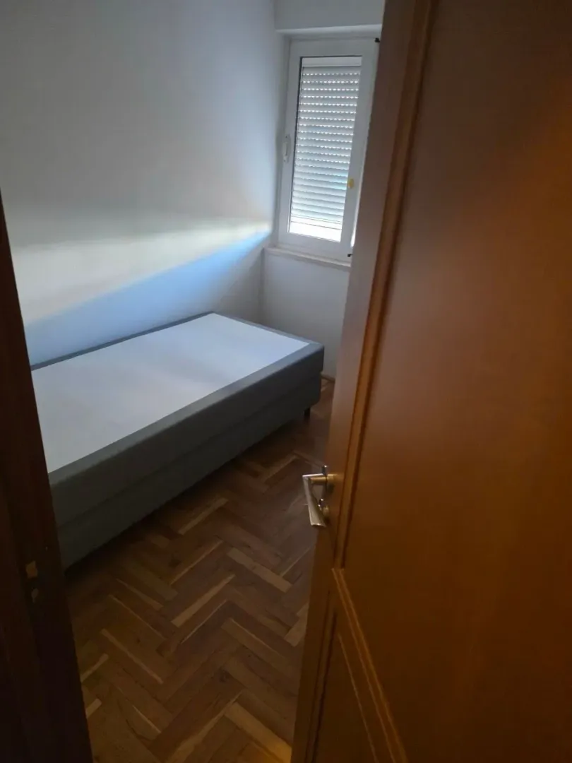 Pogled iz hodnika na manju spavaću sobu sa krevetom i prozorom.
