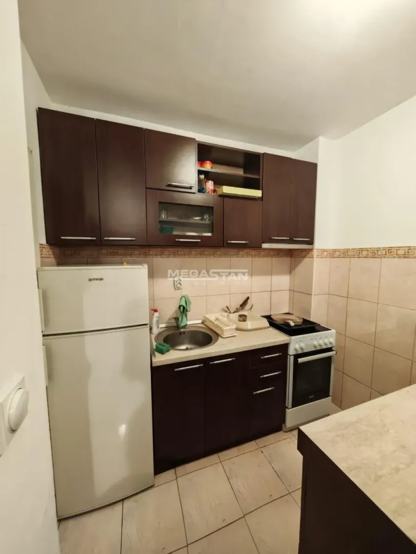 Manja kuhinja sa tamnim drvenim elementima i osnovnim kućnim aparatima.