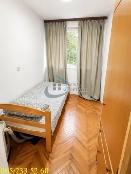 Manja spavaća soba sa krevetom, drvenim podom i prozorom sa zavesama. - image 6