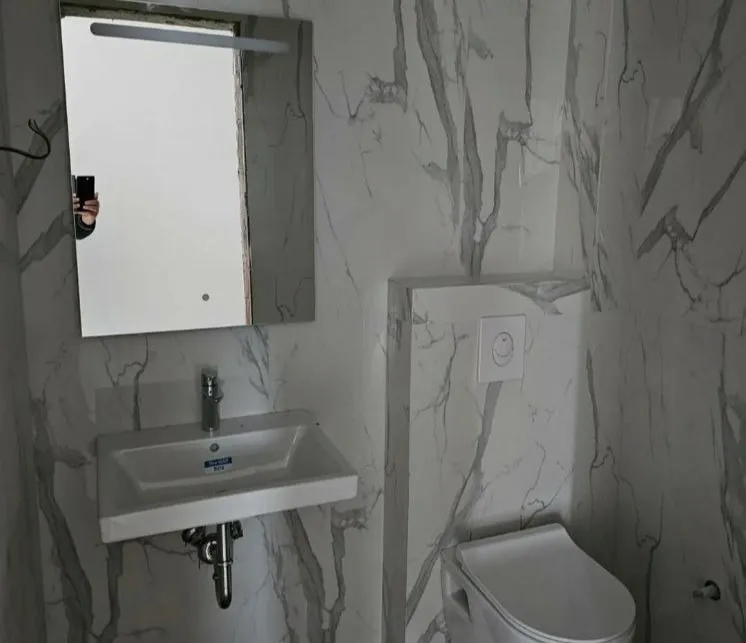 Kupatilo obloženo keramičkim pločicama sa umivaonikom i toaletom.