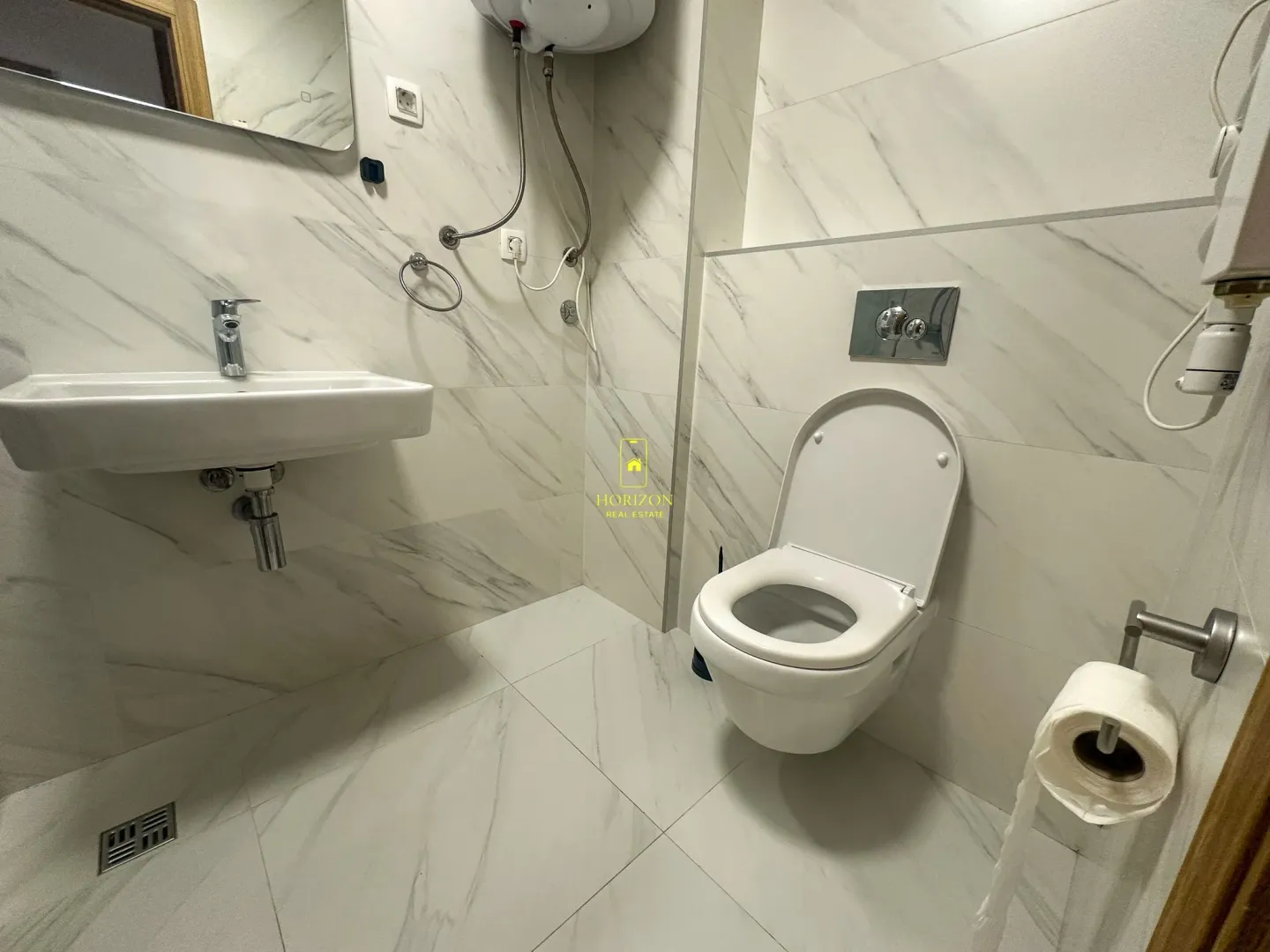 Moderno opremljeno kupatilo sa bijelim mermernim pločicama, umivaonikom i WC šoljom.