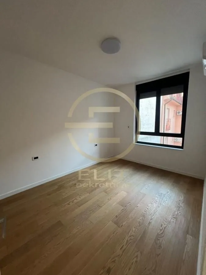 Empty room with hardwood flooring and a window.