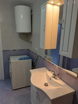 Bathroom equipped with a sink, mirrored cabinet, washing machine, and water heater. - image 11