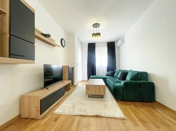 Dnevna soba sa zelenom ugaonom garniturom, televizorom i drvenim namještajem.