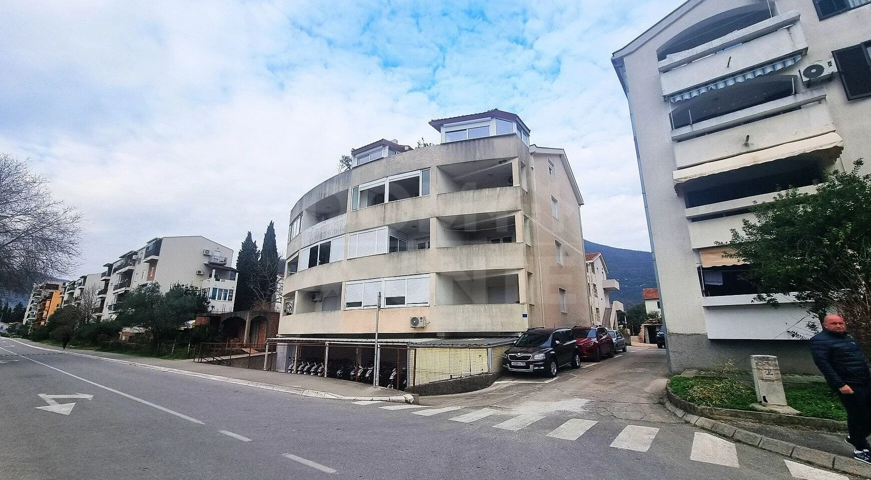 Pogled sa ulice na stambenu zgradu sa terasama i parkingom.