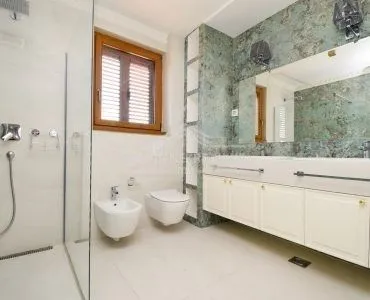 Moderno kupatilo sa tuš kabinom, bideom i velikim ogledalom.