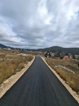 Asfaltni put koji vodi kroz naselje sa vikendicama i brdovitim pejzažem u pozadini. - image 3