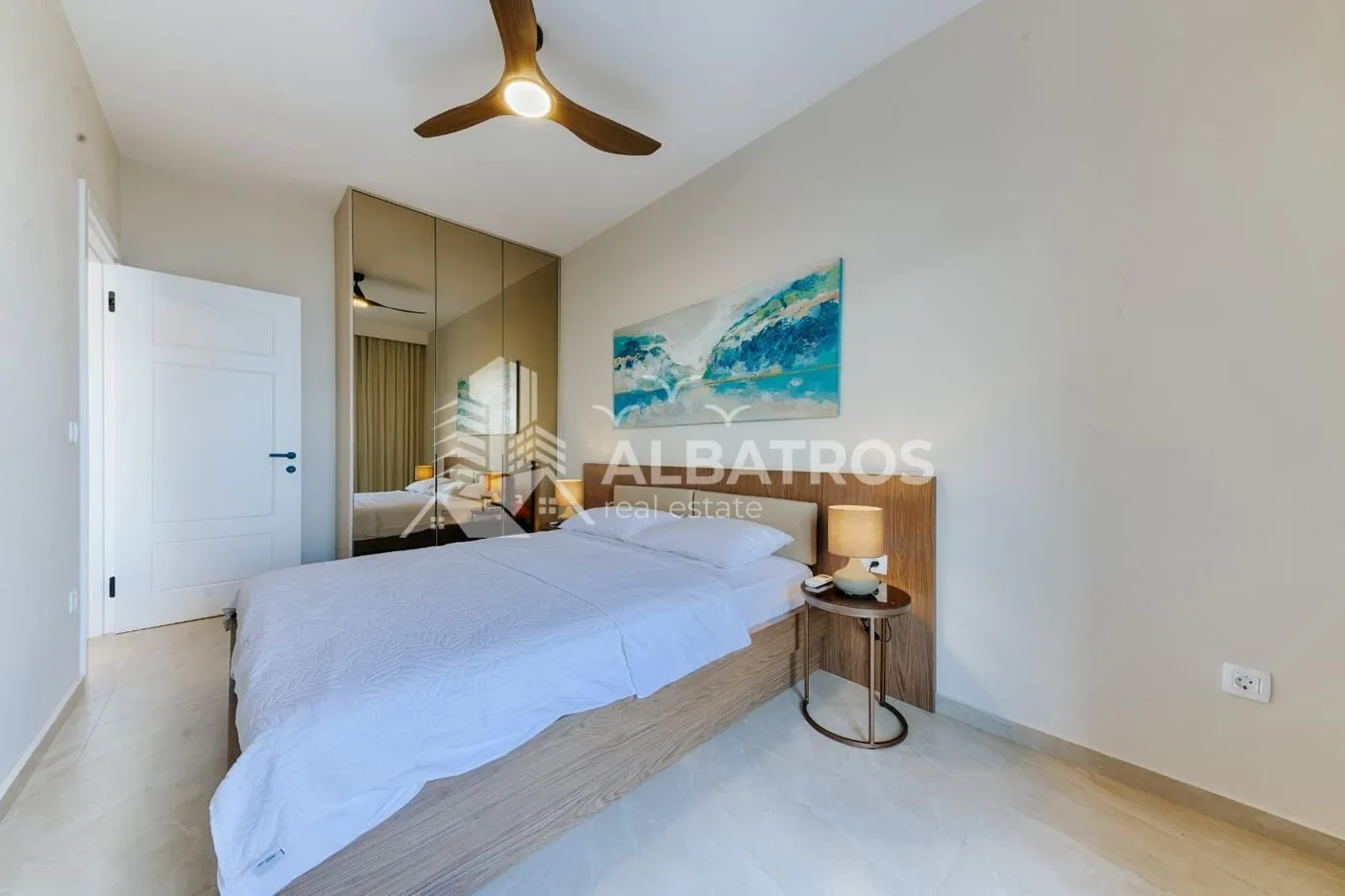 Modern bedroom with a double bed, mirrored built-in wardrobe, and ceiling fan.