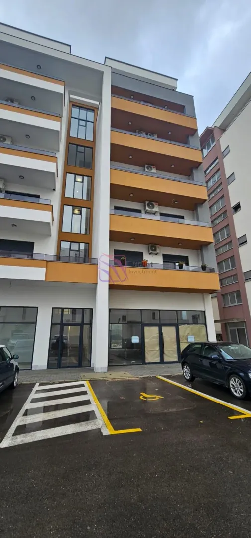 Pogled na spoljašnjost moderne stambene zgrade sa parkingom i poslovnim prostorom u prizemlju.