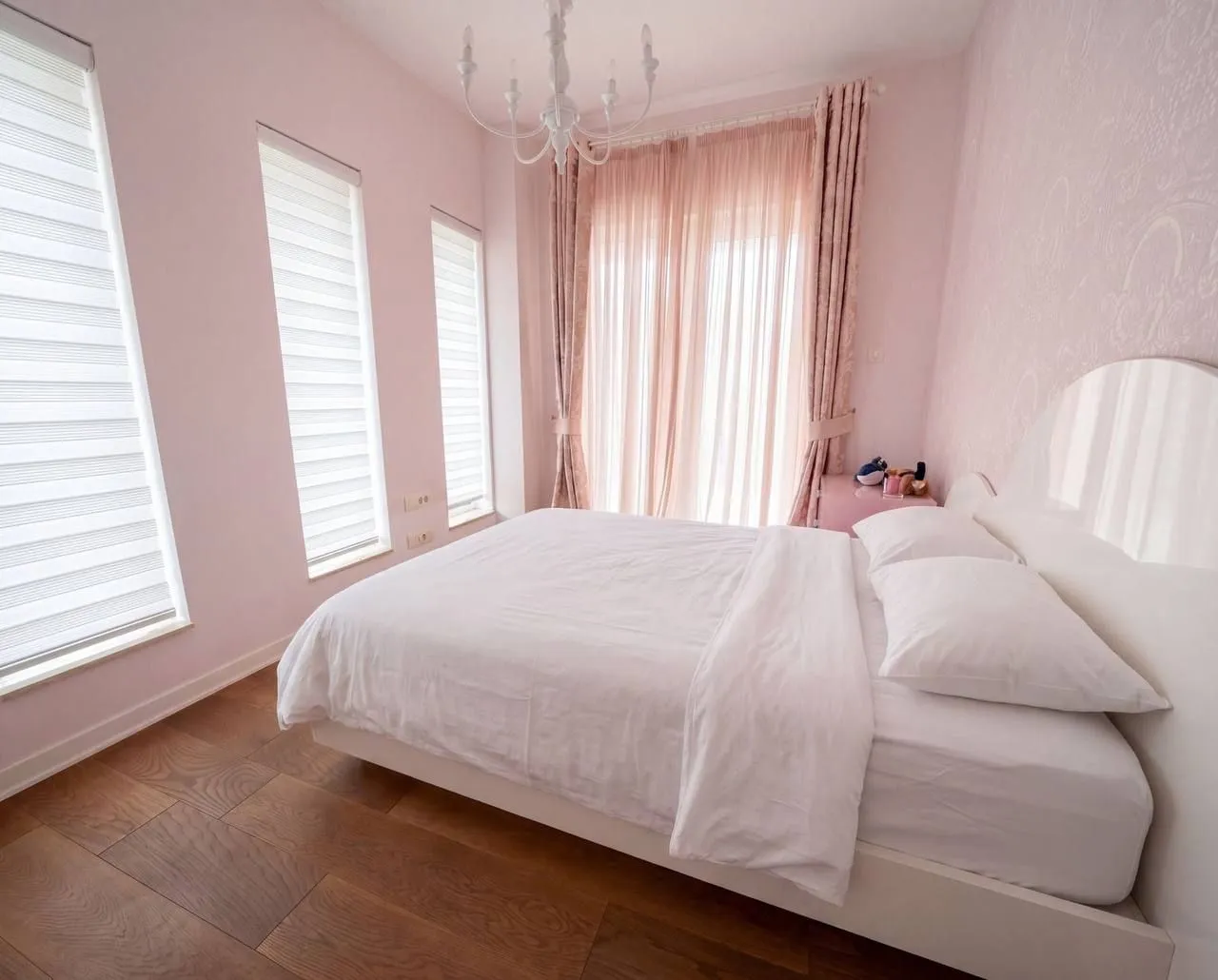 Bright bedroom with a double bed, pink details, and windows.
