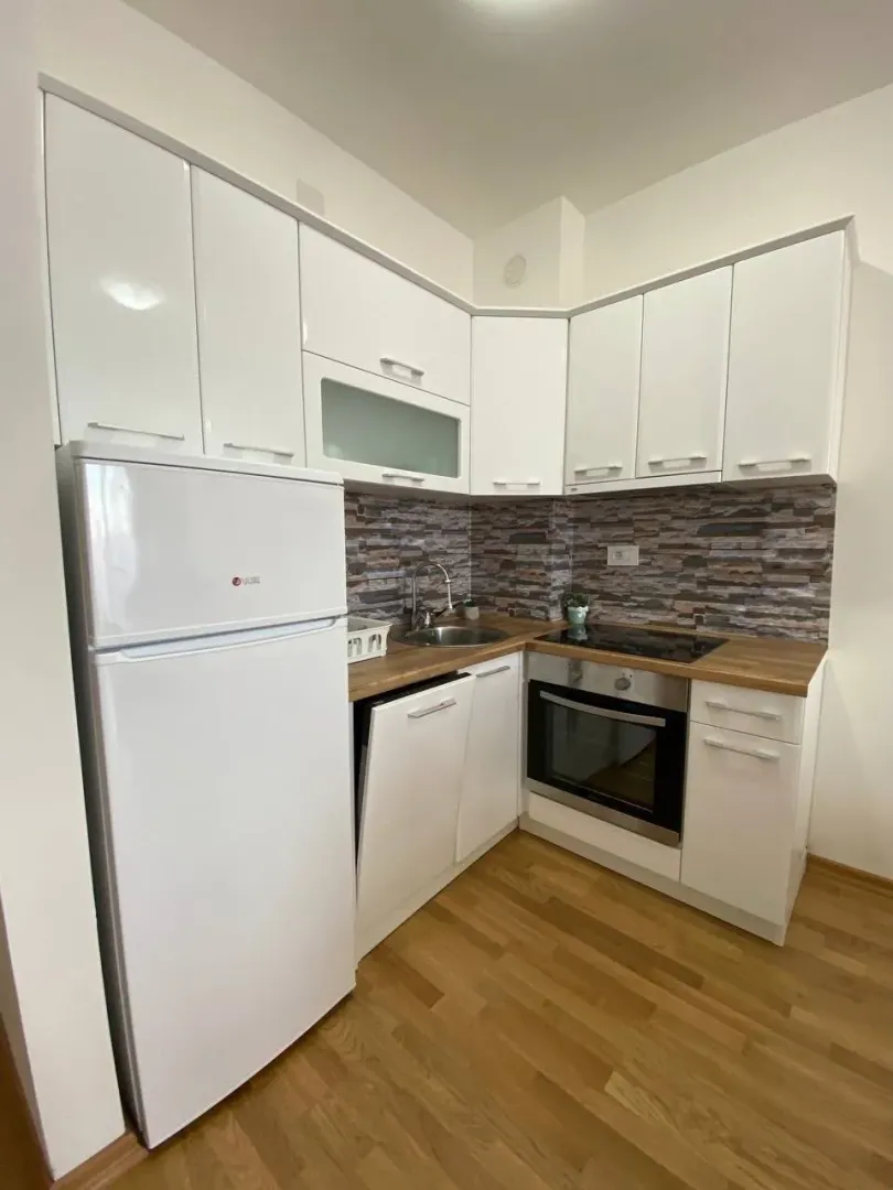 Small white kitchen with a wooden countertop and built-in appliances.