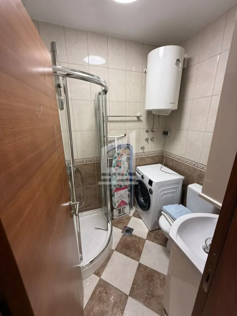 Small bathroom with a shower cabin, washbasin, toilet, and washing machine.