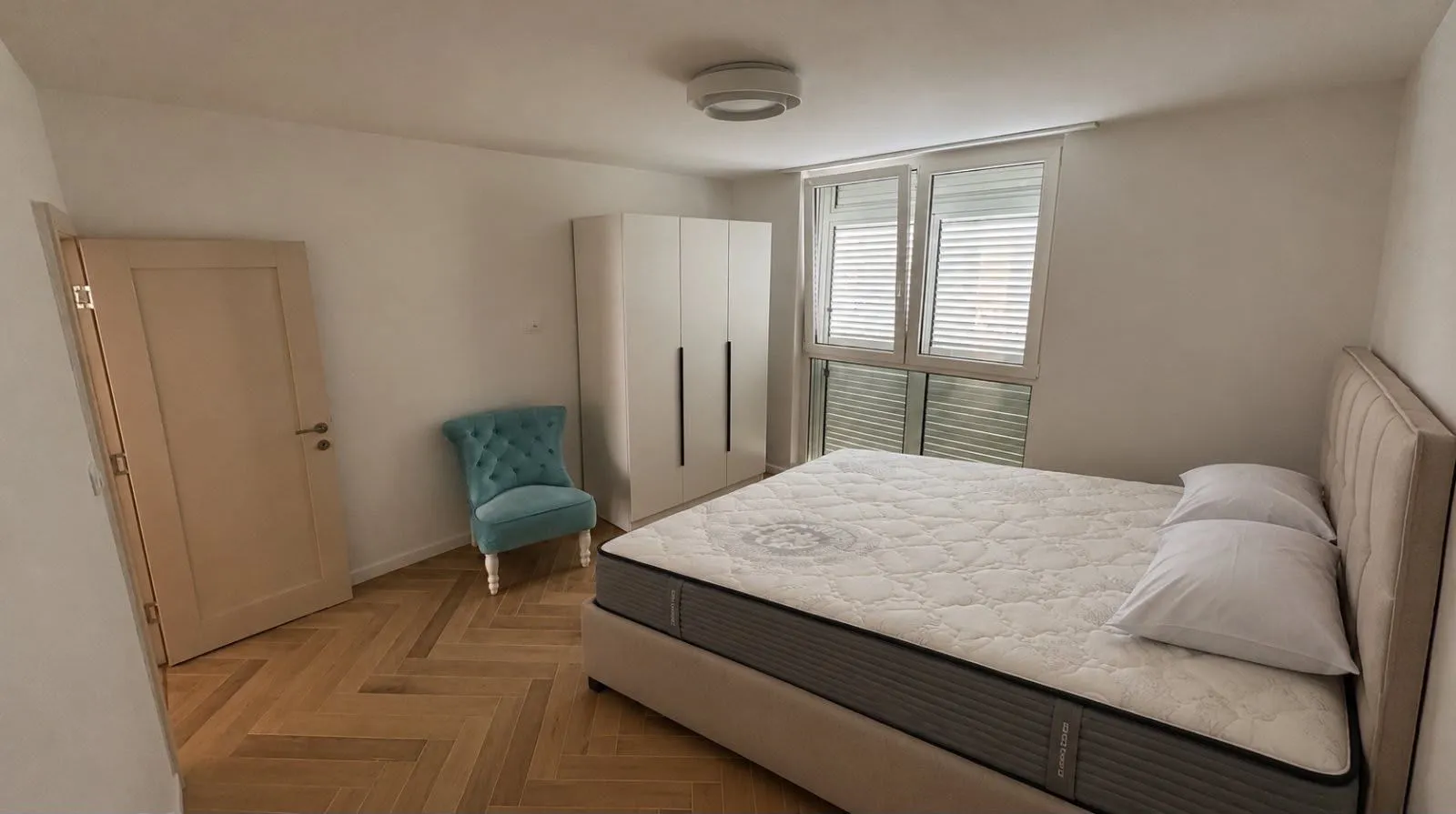 Bedroom with a double bed, wardrobe, blue armchair, and parquet flooring.